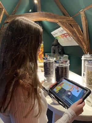 Photo d'une jeune fille qui tient un écran tactile sur lequel est afficher le visio-guide au Choco Story Brussels.